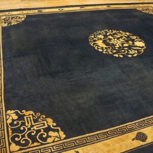 A deep blue rug featuring a central gold floral medallion and wide, patterned gold borders rests on a wood floor.