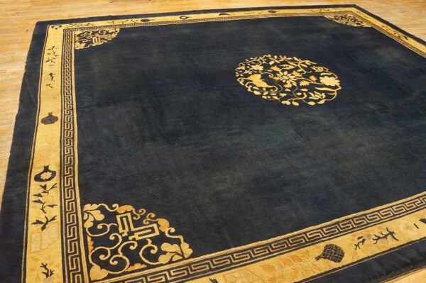 A deep blue rug featuring a central gold floral medallion and wide, patterned gold borders rests on a wood floor.