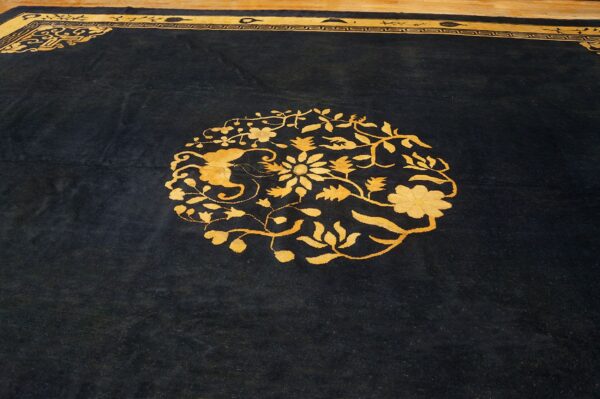 Black high-pile rug with a bright yellow floral medallion and decorative key border on wood floor.