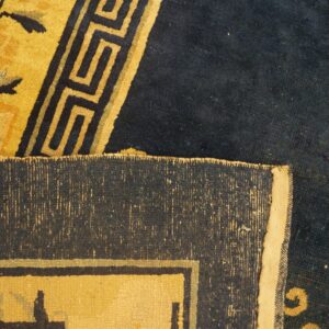 Navy and yellow rug detail featuring floral and Greek key motifs, with the folded woven edge visible.