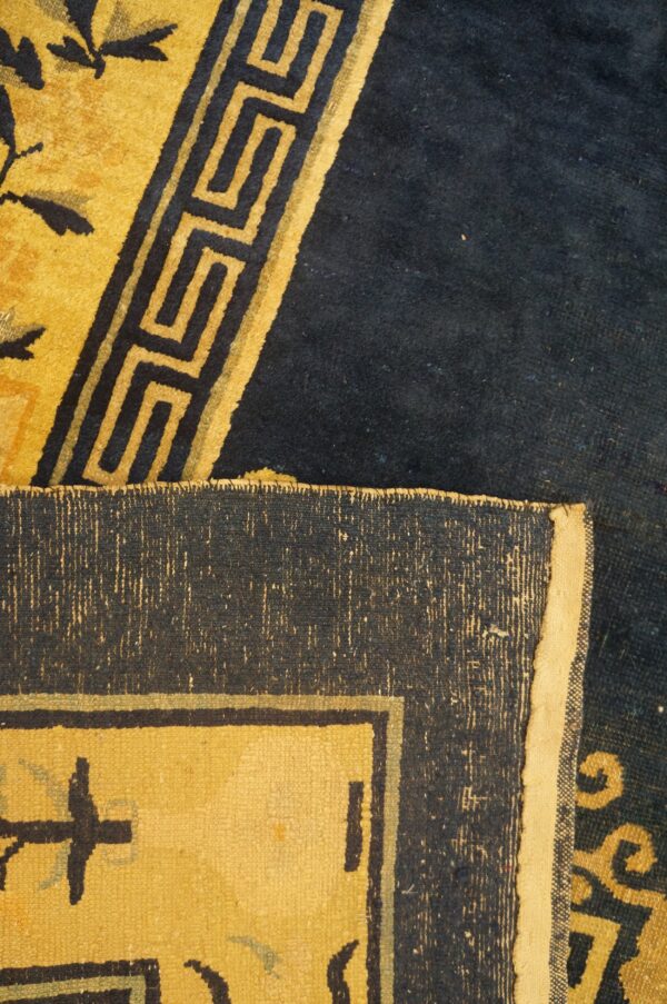 Navy and yellow rug detail featuring floral and greek key motifs, with the folded woven edge visible.