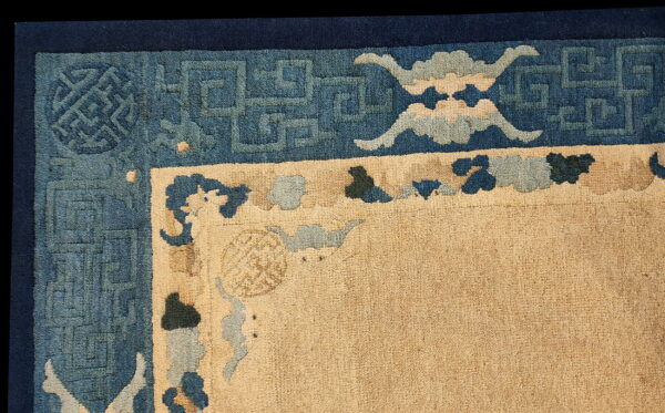 Close-up of a beige rug corner bordered by dark blue geometric fretwork and stylized cloud motifs.