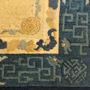 The rug detail features a golden yellow pile field framed by a deep blue geometric meander border.