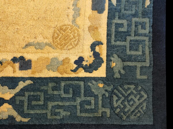 The rug detail features a golden yellow pile field framed by a deep blue geometric meander border.