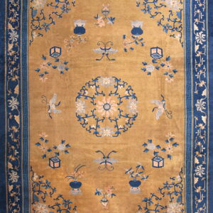 Gold rug with dark blue borders and scattered medallions, vases, butterflies, and flowering branches.