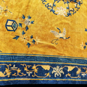 Gold and blue rug detail showing central floral motifs and a border with Greek key and scrolling patterns.
