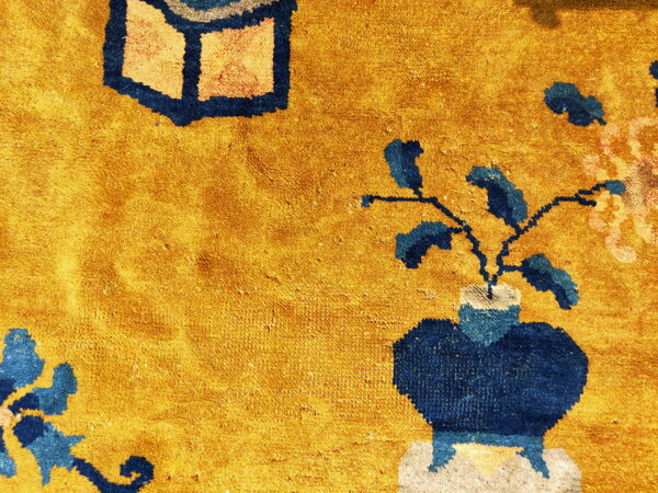 Plush golden yellow rug texture with a navy blue vase motif holding blue and peach stylized flowers.