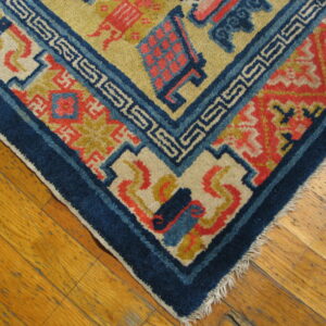 Geometric rug in navy, coral, and yellow with Greek key pattern, laid on glossy wood planks.