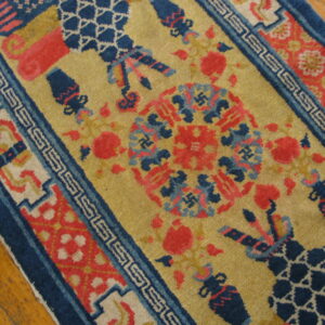 Mustard gold rug with navy blue and coral motifs, geometric borders, lying on distressed wood planks.