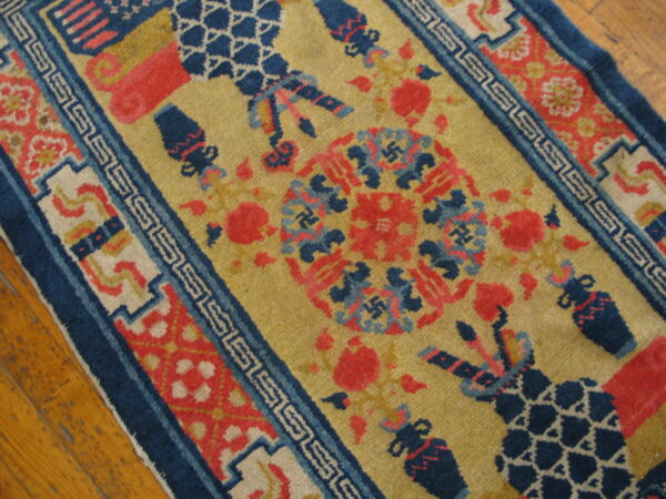 Mustard gold rug with navy blue and coral motifs, geometric borders, lying on distressed wood planks.
