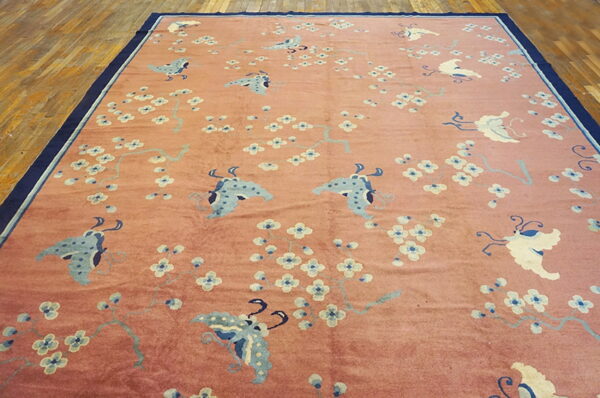 Pink rug with light blue butterflies and white flowers, dark blue border, placed on wood floor.