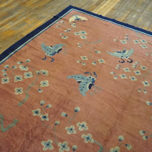 A rose colored rug with blue butterflies and blossoms rests on hardwood, bordered in dark blue.