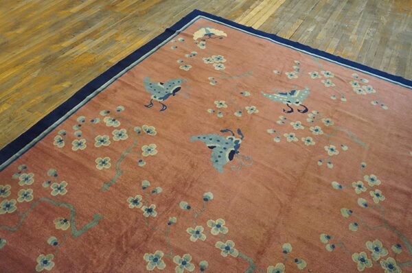 A rose colored rug with blue butterflies and blossoms rests on hardwood, bordered in dark blue.