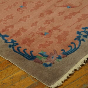 Pink and salmon patterned rug corner with a scrolling blue and multicolored floral border on wood floor.