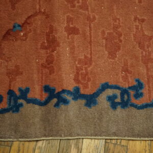 Burnt orange rug features subtle motifs above a dark blue border section and tan edge on exposed wood planks.