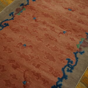 Terracotta rug with faint floral pattern and bold blue border scrollwork rests on hardwood flooring.