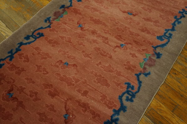 Terracotta rug with faint floral pattern and bold blue border scrollwork rests on hardwood flooring.