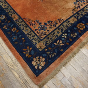 Orange high-pile rug corner with blue and brown floral borders rests on rustic gray plank flooring.