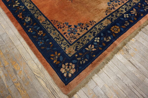 Orange high-pile rug corner with blue and brown floral borders rests on rustic gray plank flooring.