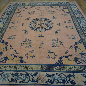 Low-pile pink rug with blue and yellow floral motifs and complex borders on a distressed wood floor.
