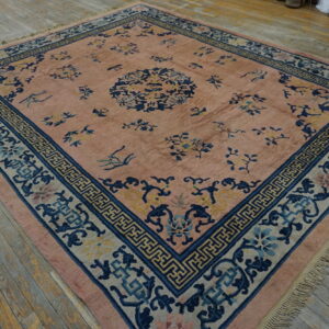 Muted pink rug with blue and yellow floral motifs and patterned borders on gray wooden planks.