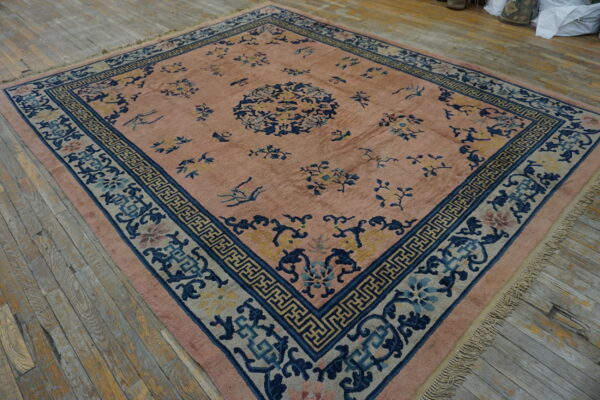 Muted pink rug with blue and yellow floral motifs and patterned borders on gray wooden planks.