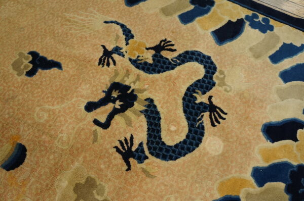Vintage light coral color chinese cloud band dragon motif peking rug 3 High-pile rug featuring a navy dragon and yellow accents on a peachy orange field near wood flooring.