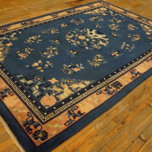 Blue floral pattern rug with a wide peach and dark blue meander border on worn wood planks.