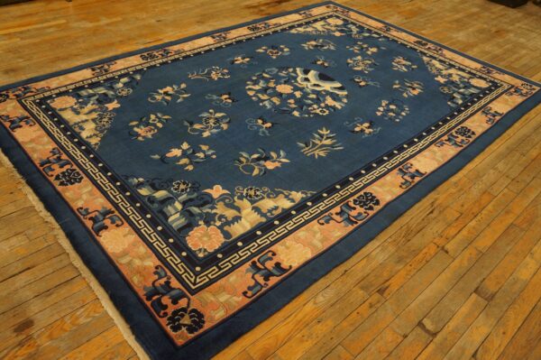 Blue floral pattern rug with a wide peach and dark blue meander border on worn wood planks.
