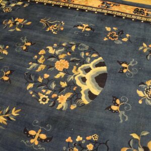 Dark blue high-pile rug with a detailed gold floral center and geometric border on a wood floor.