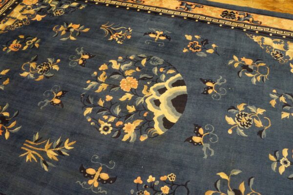 Dark blue high-pile rug with a detailed gold floral center and geometric border on a wood floor.