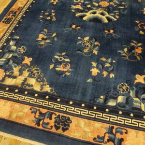 Dark blue rug featuring gold and peach floral motifs and a Greek key border over wood flooring.