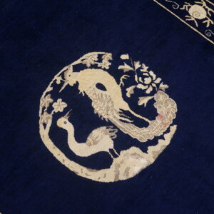 Dark blue rug detail showing a beige medallion with two stylized birds and a patterned border.