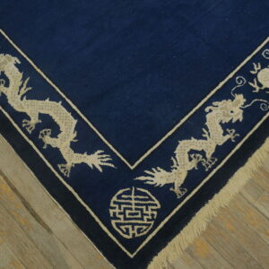 Corner of a dark blue rug with a beige border featuring stylized dragons on distressed wood.