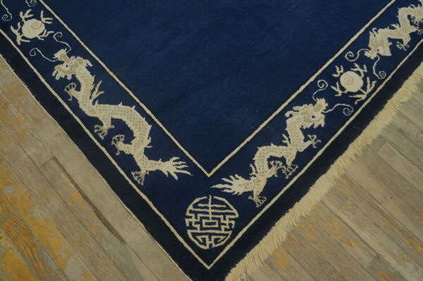 Corner of a dark blue rug with a beige border featuring stylized dragons on distressed wood.