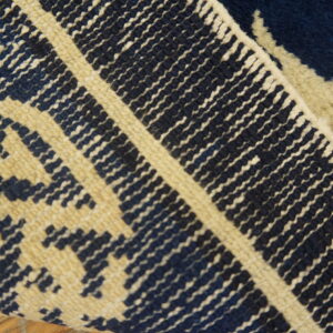 Close-up of a navy blue and beige patterned rug that is folded over, showing high pile texture.