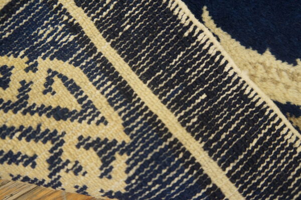 Close-up of a navy blue and beige patterned rug that is folded over, showing high pile texture.