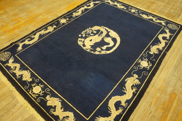 Navy blue and light beige dragon rug on worn, wide plank wooden flooring.