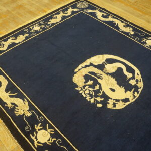 A navy blue rug with a central beige bird medallion and a wide border featuring dragons rests on wood flooring.