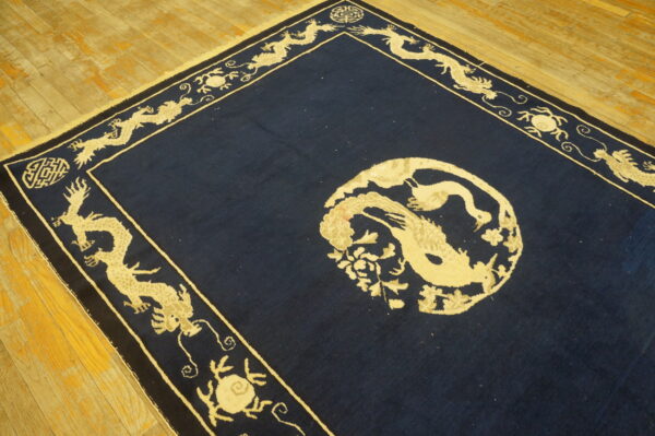 A navy blue rug with a central beige bird medallion and a wide border featuring dragons rests on wood flooring.