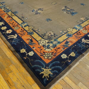 Muted taupe rug corner with detailed navy, orange, and yellow floral borders resting on hardwood planks.