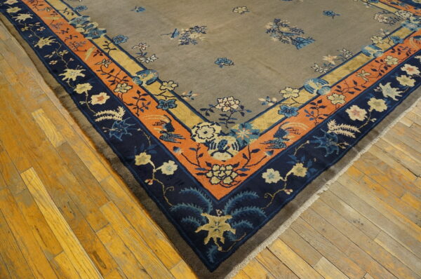 Muted taupe rug corner with detailed navy, orange, and yellow floral borders resting on hardwood planks.