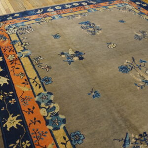 Gray rug with blue and cream scattered florals, detailed navy and orange multi-layered borders on wood floor.