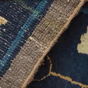 The detailed reverse of the rug shows woven stripes next to the front with orange, navy, and cream floral motifs.