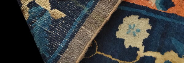 The detailed reverse of the rug shows woven stripes next to the front with orange, navy, and cream floral motifs.