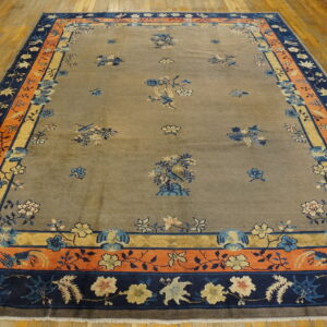 High-pile taupe rug featuring blue birds and flowers, surrounded by detailed orange and dark blue borders on wood floors.