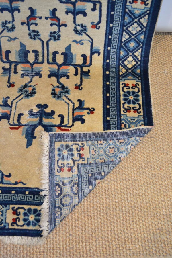 Beige rug with navy and blue floral motifs folded back, showing fringe over a textured tan rug.