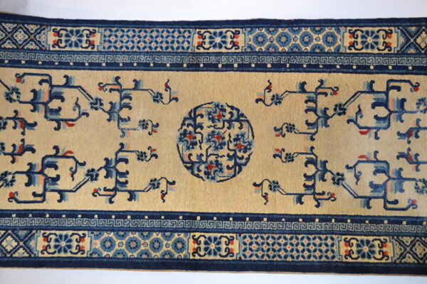A tan rug runner features navy blue abstract vines and a central medallion, framed by a thick geometric border.