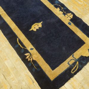 Antique dark blue runner rug with thick tan borders and floral motifs on wood floor.