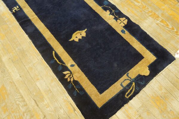 Antique dark blue runner rug with thick tan borders and floral motifs on wood floor.